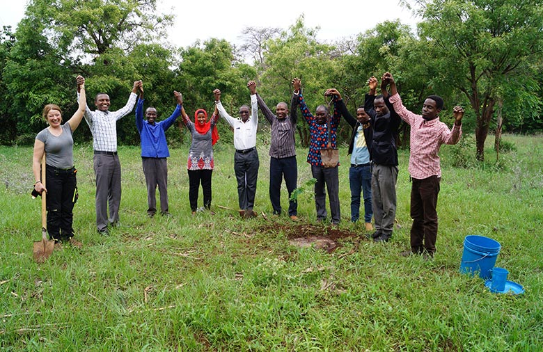 Un groupe, debout sur une pelouse, lève les bras en riant.